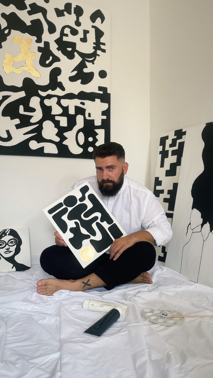 Greek artist Giorgos in his studio, surrounded by minimalist paintings inspired by Greek heritage, history, and modern social themes.