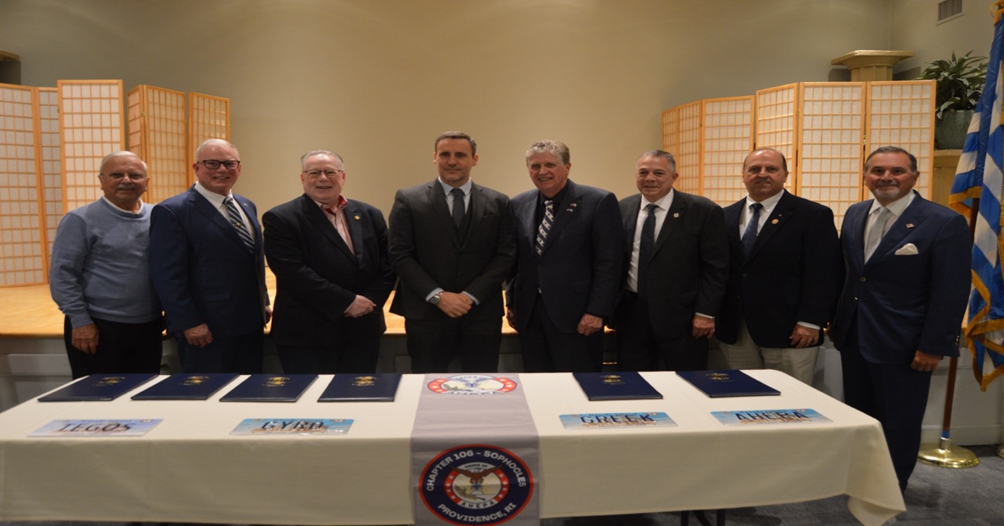 License plates displayed with Ahepa banner and legislation binders. Left to Right Past Sophocles Chapter 106 Ahepa President Lakis Andriotis, State Representative Joseph M. McNamara, Sophocles 106 chapter President George Coclin, Consul General Greece Boston Symeon Tegos, Rhode Island Governor Dan McKee, State Senator Lou Raptakis, Past Supreme President Dr. John Grossomanides and Past Ahepa 121-chapter President George Demopoulos