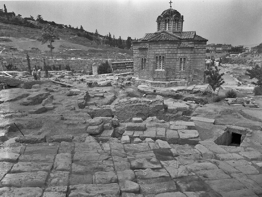 Σε πρώτο πλάνο η λιθόστρωτη Οδός των Παναθηναίων, στο κέντρο τα κατάλοιπα του υδρόμυλου
